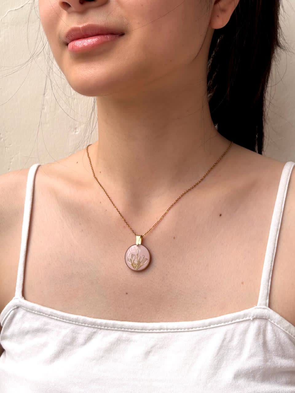 Kalung oval berwarna pink dikenakan di leher