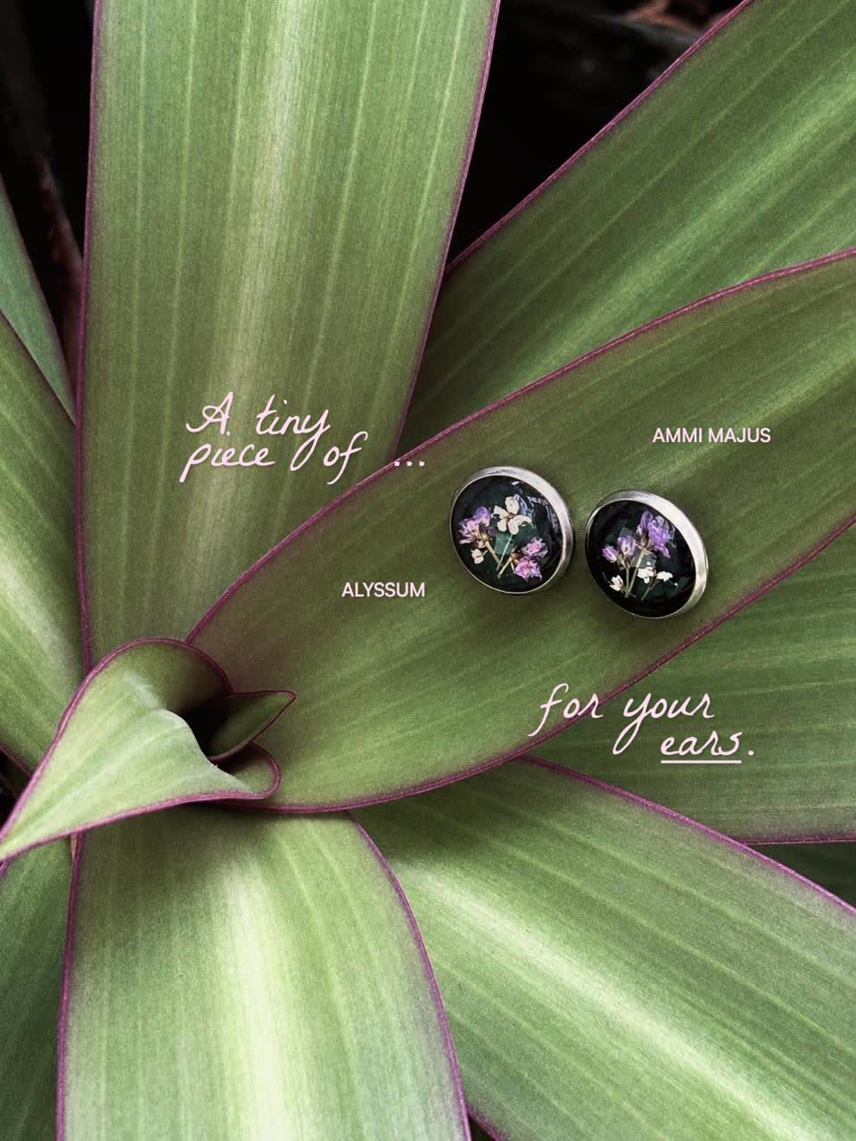 Anting bunga ungu dan putih di antara dedaunan